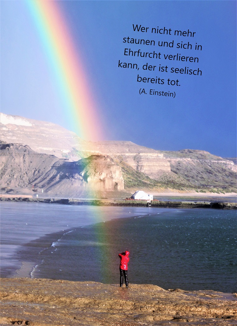 Mensch unter einem Regenbogen am Meer